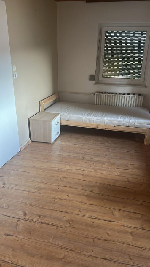 Einzelbett mit Nachttisch und Fenster für natürliches Licht.