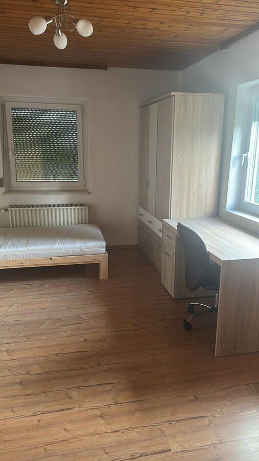 Einzelbett, großer Kleiderschrank, großzügiger Schreibtisch mit ergonomischem Stuhl, Holzboden, natürliches Licht.